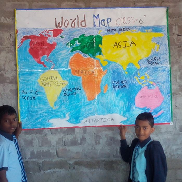 Two students holding up a large hand-drawn and hand-coloured world map labelled with continents and oceans against a brick wall