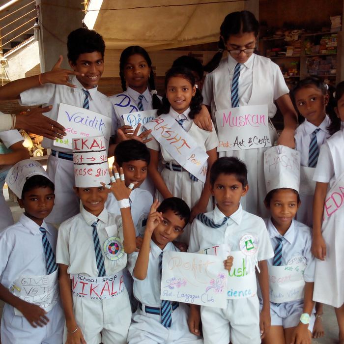 A large group of uniformed students wearing hand-lettered paper sashes and caps naming candidates and the school posts they are standing for