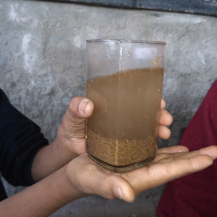 A child's hands holding a glass of muddy water in which sediment has settled into a distinct layer at the bottom