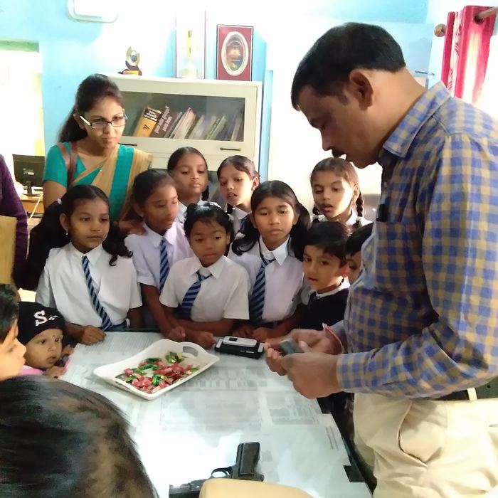 A police officer showing equipment on a table to a group of young students gathered around him inside a station office