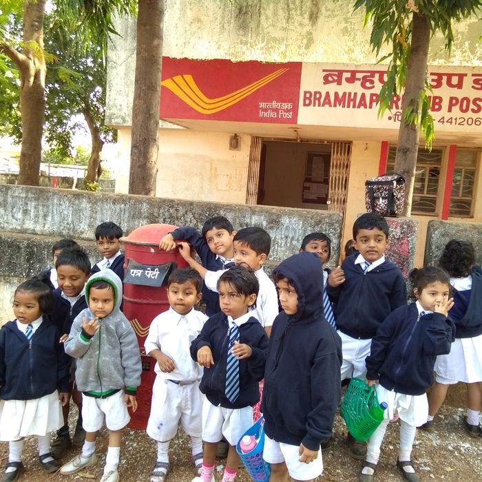 Young students in uniform standing around a red India Post letter box outside the Bramhapuri sub post office