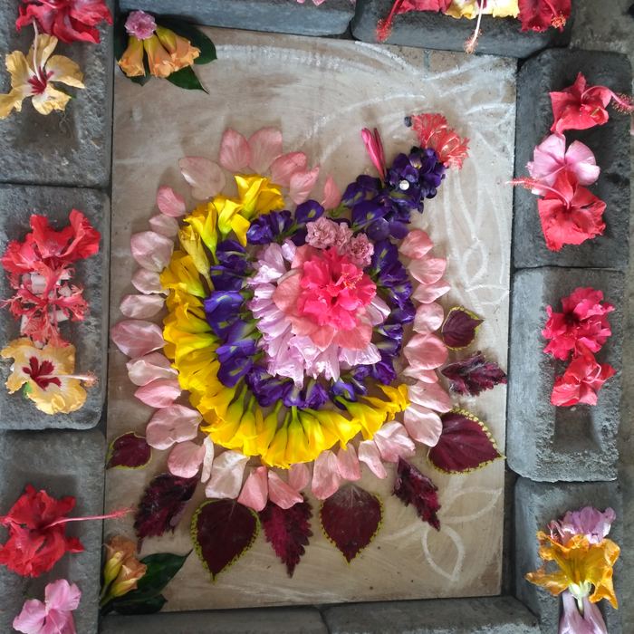 A rangoli of concentric rings made from whole pink, yellow and purple blooms on a pale slab, framed by bricks each holding hibiscus flowers