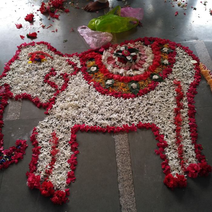 A large elephant rangoli filled with white jasmine and outlined in red flowers, laid across a grey tiled floor