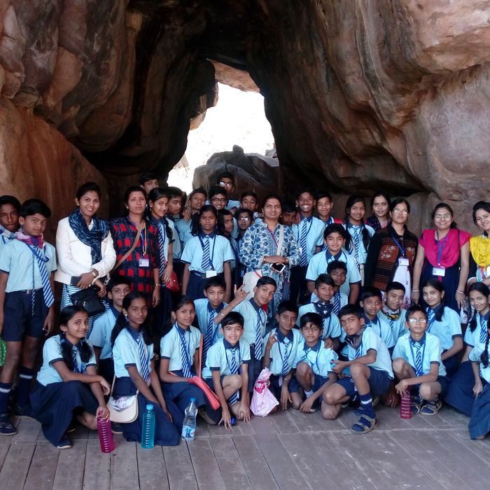 The whole school group and their teachers posed together under the wide mouth of a prehistoric sandstone rock shelter