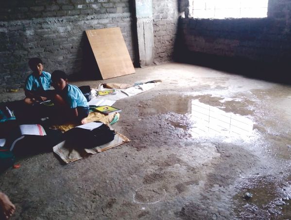 Students studying on the floor of an unfinished classroom with bare brick walls