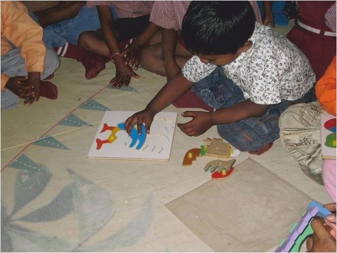 A young child working on a shape puzzle on the classroom floor