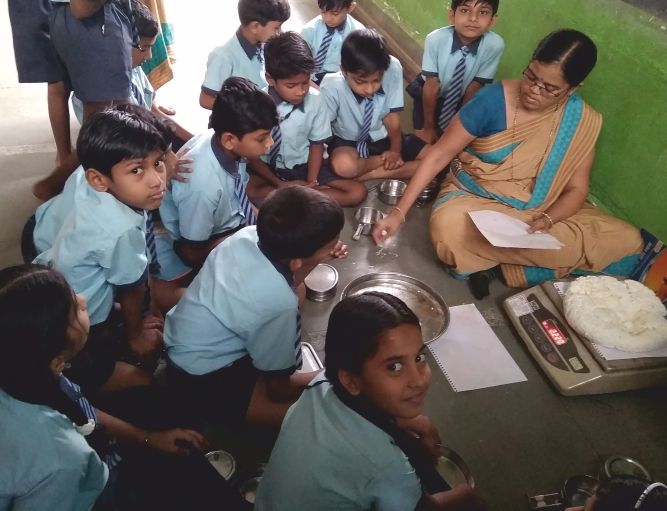 A teacher and students gathered around a weighing scale during a classroom experiment