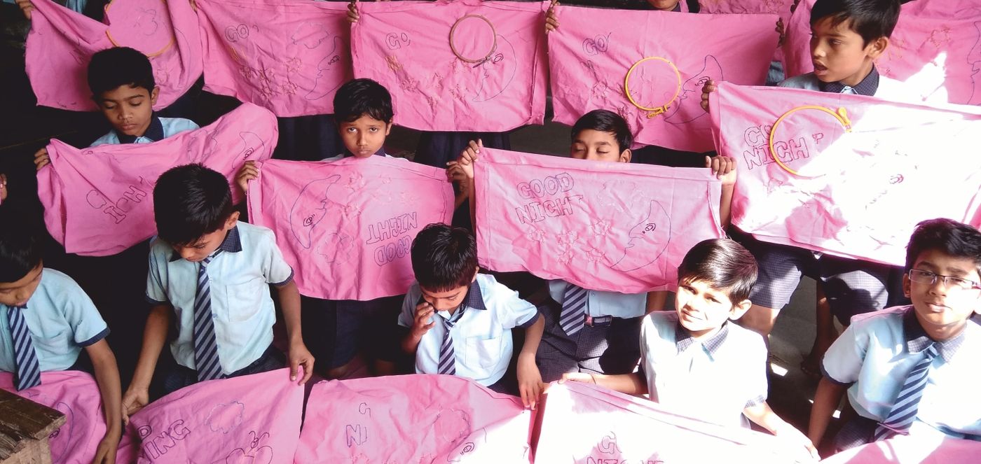 Students holding up pink cloth pieces they have embroidered